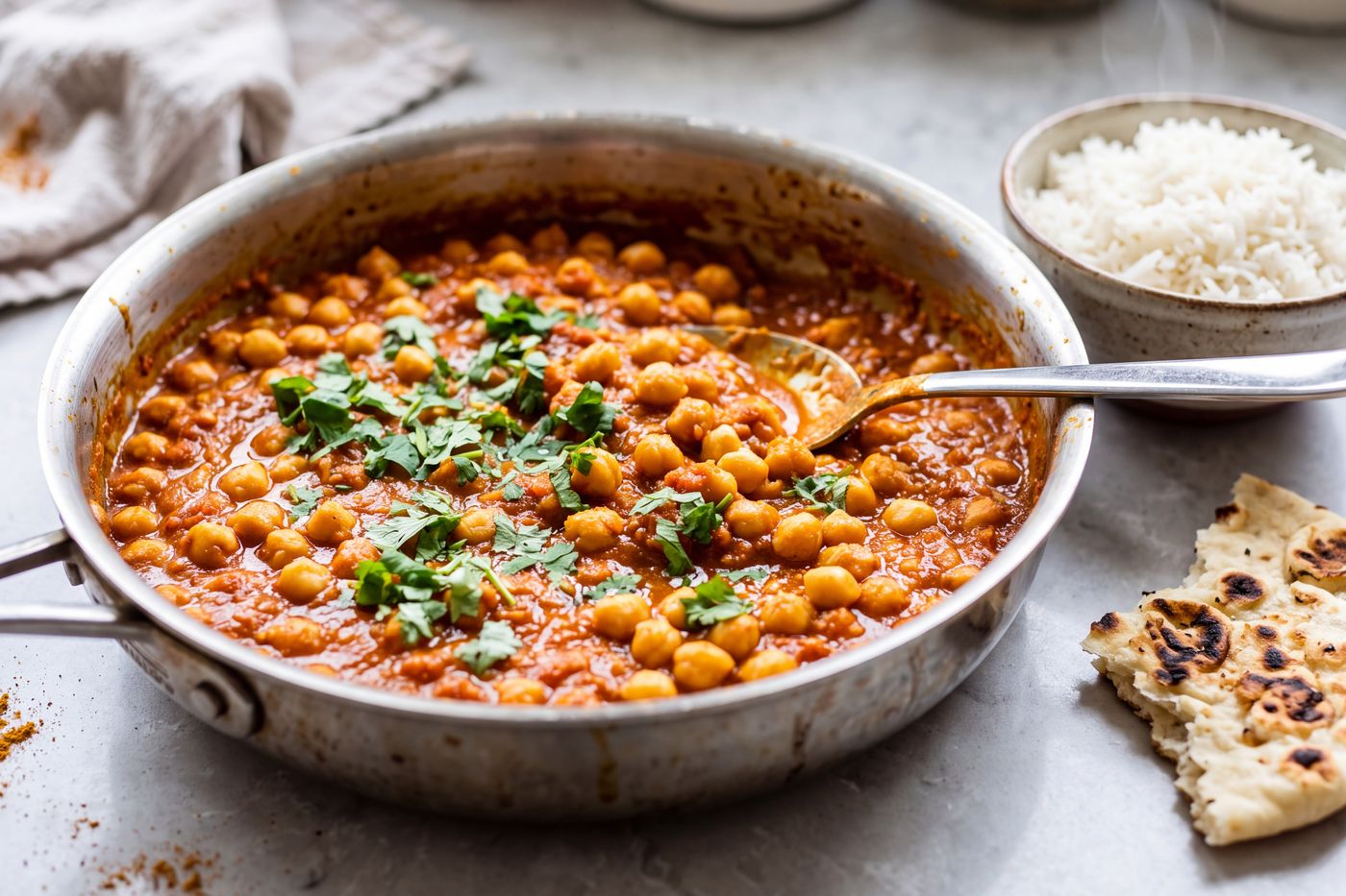 A pan of chana masala topped with cilantro, with rice and naan beside it