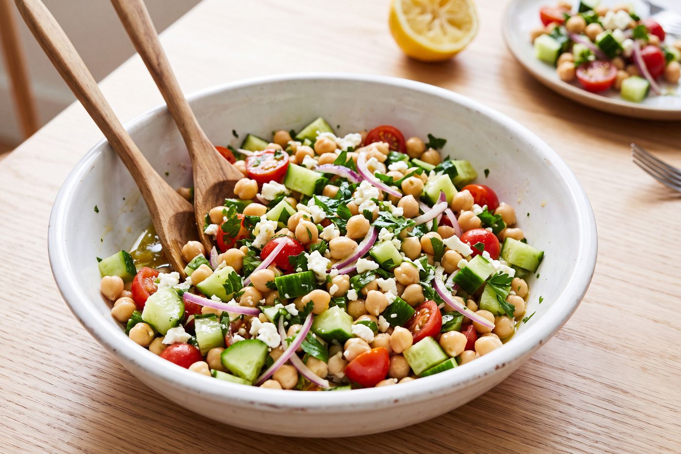 A bowl of garbanzo bean salad with cucumber, tomato, red onion, parsley and feta